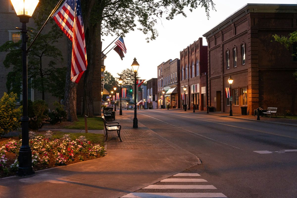 A small-town main street at dusk with shops lit up