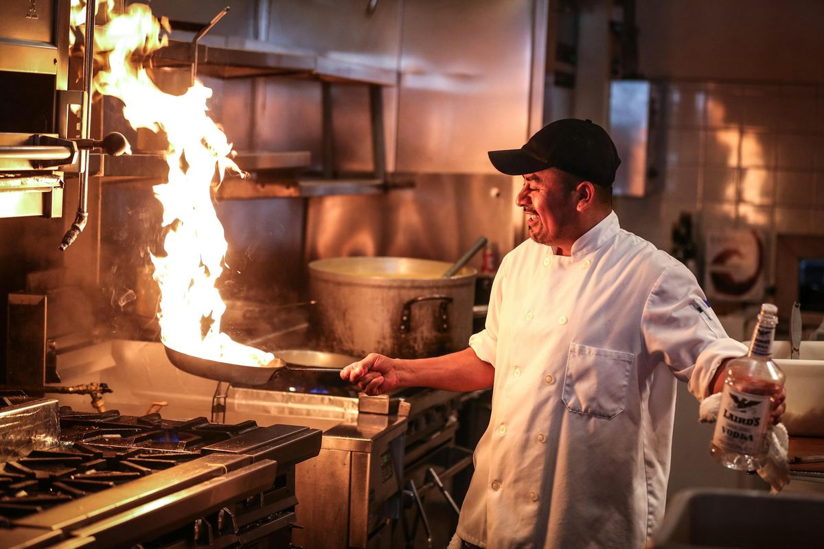 A chef working over a flaming pan in a restaurant kitchen